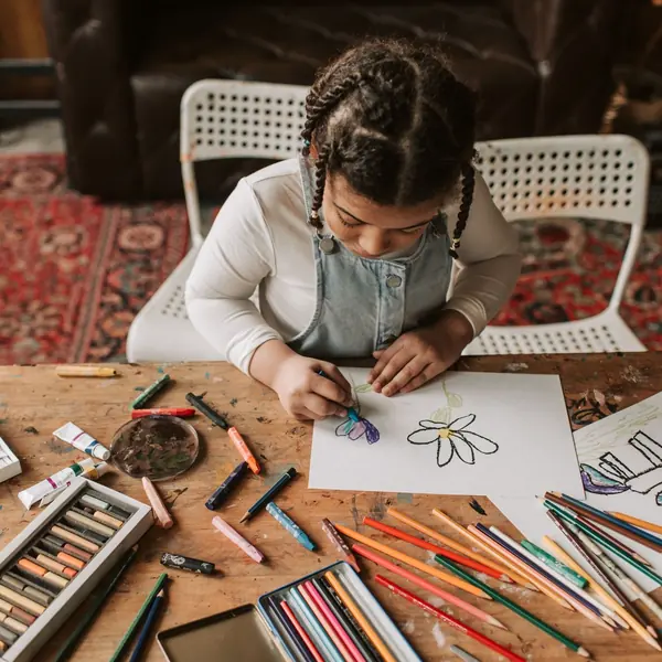 Girl coloring a drawing with crayons at a table